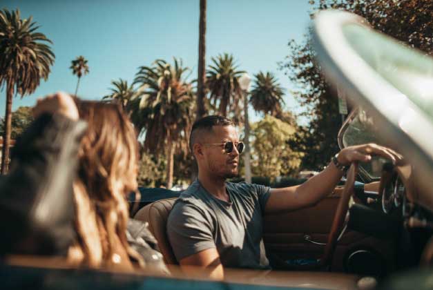 man driving convertable car with palm trees in background.